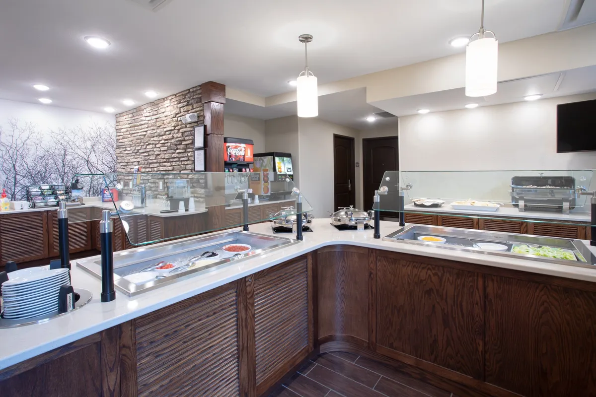 This image showcases a vibrant breakfast buffet area filled with enticing food displays. The setting is bright and welcoming, with a decorative wall featuring tree motifs adding to the cozy, inviting atmosphere. Guests are seen enjoying breakfast and socializing, reflecting the communal dining experience.