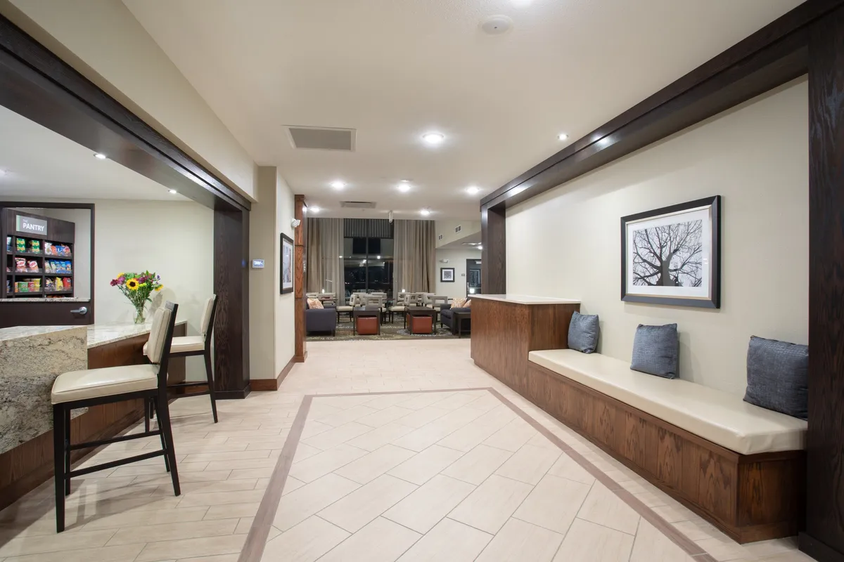 A comfortable and inviting indoor lounge area featuring a modern seating arrangement, an art piece on the wall, and a food and beverage section. The space is designed for socializing, relaxing, and enjoying casual snacks or drinks, echoing the feel of a hotel reception area.