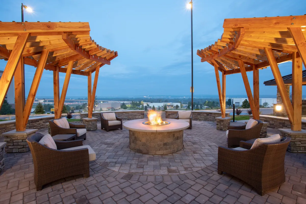 An exterior communal area is shown, featuring a cozy fire pit surrounded by wooden pergolas and ample seating. Guests gather to relax, socialize, and unwind, with the warm lighting suggesting evening gatherings or post-event relaxation.