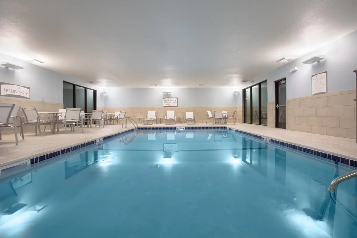 An inviting indoor swimming pool area with comfortable lounge chairs lining the poolside. Large windows fill the space with natural light, creating a serene atmosphere ideal for relaxing after a day of exploring.