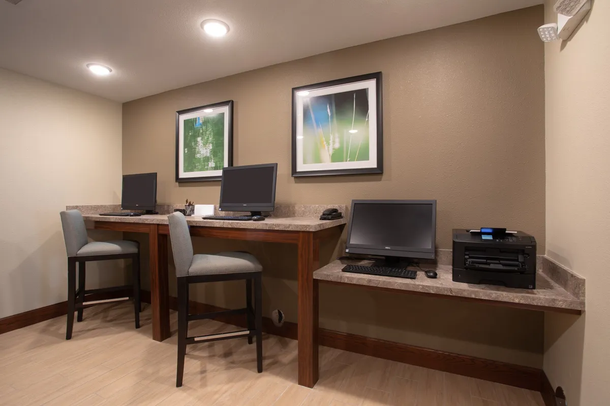A serene business center with computers, a wooden desk, printer, and framed artwork. The layout is functional and peaceful, offering guests a convenient workspace to stay productive while away from home.