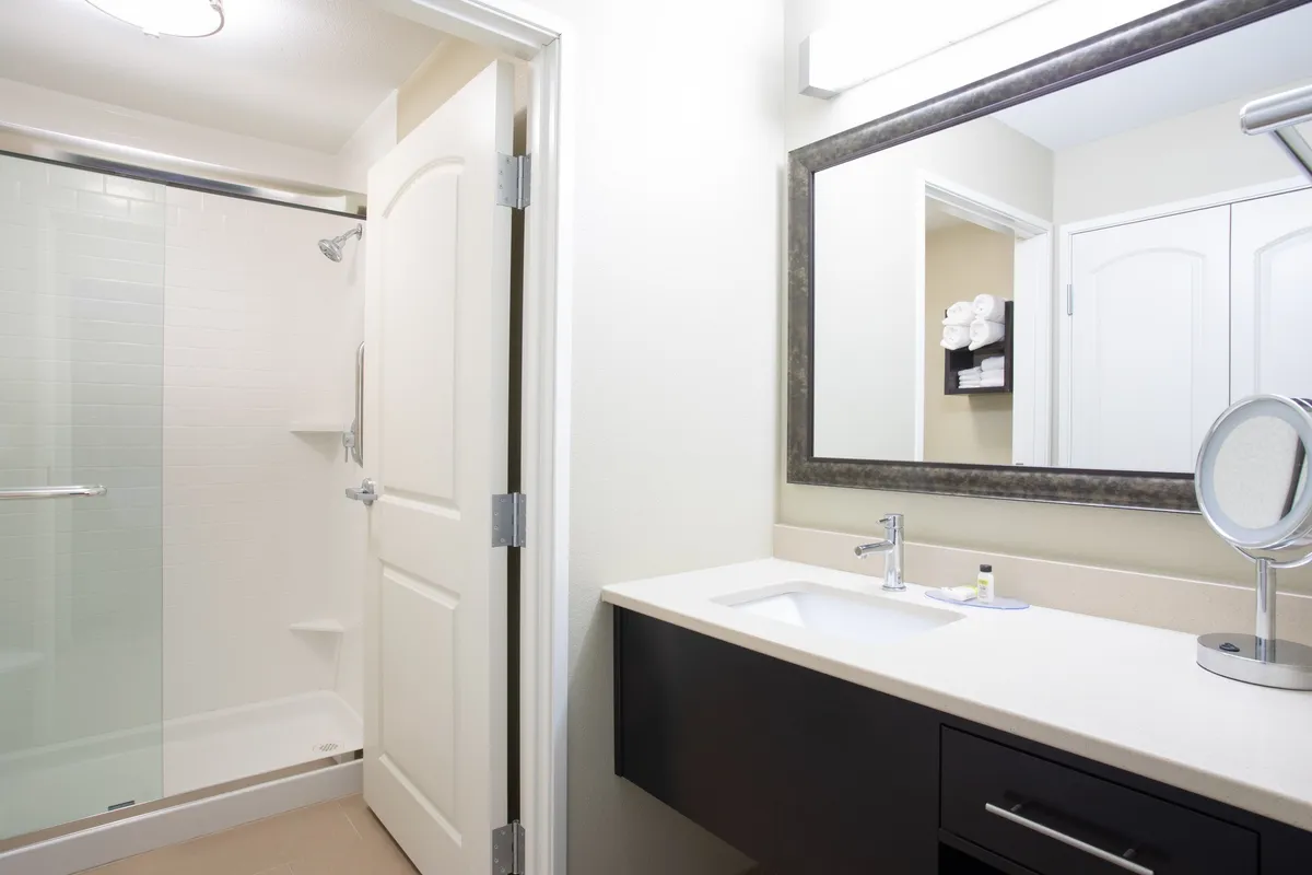 Captured here is a modern bathroom featuring a glass-enclosed shower, a sleek vanity with a large mirror, and towels neatly arranged on a rack. The space feels refreshing and serene, with an emphasis on comfort and cleanliness.
