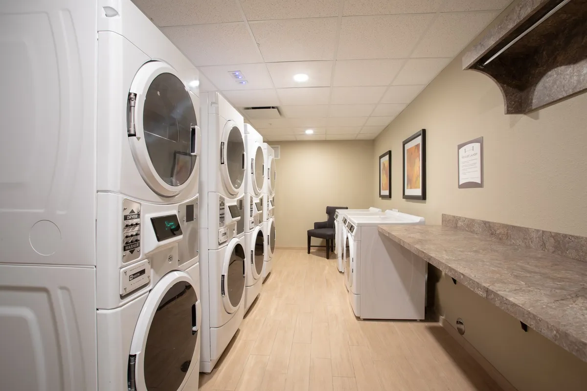 A practical laundry area with stacked washer and dryer units, counter space, and a small seating section. The setting is clean, accessible, and designed to provide convenience for guests who value consistent amenities and home-like features.