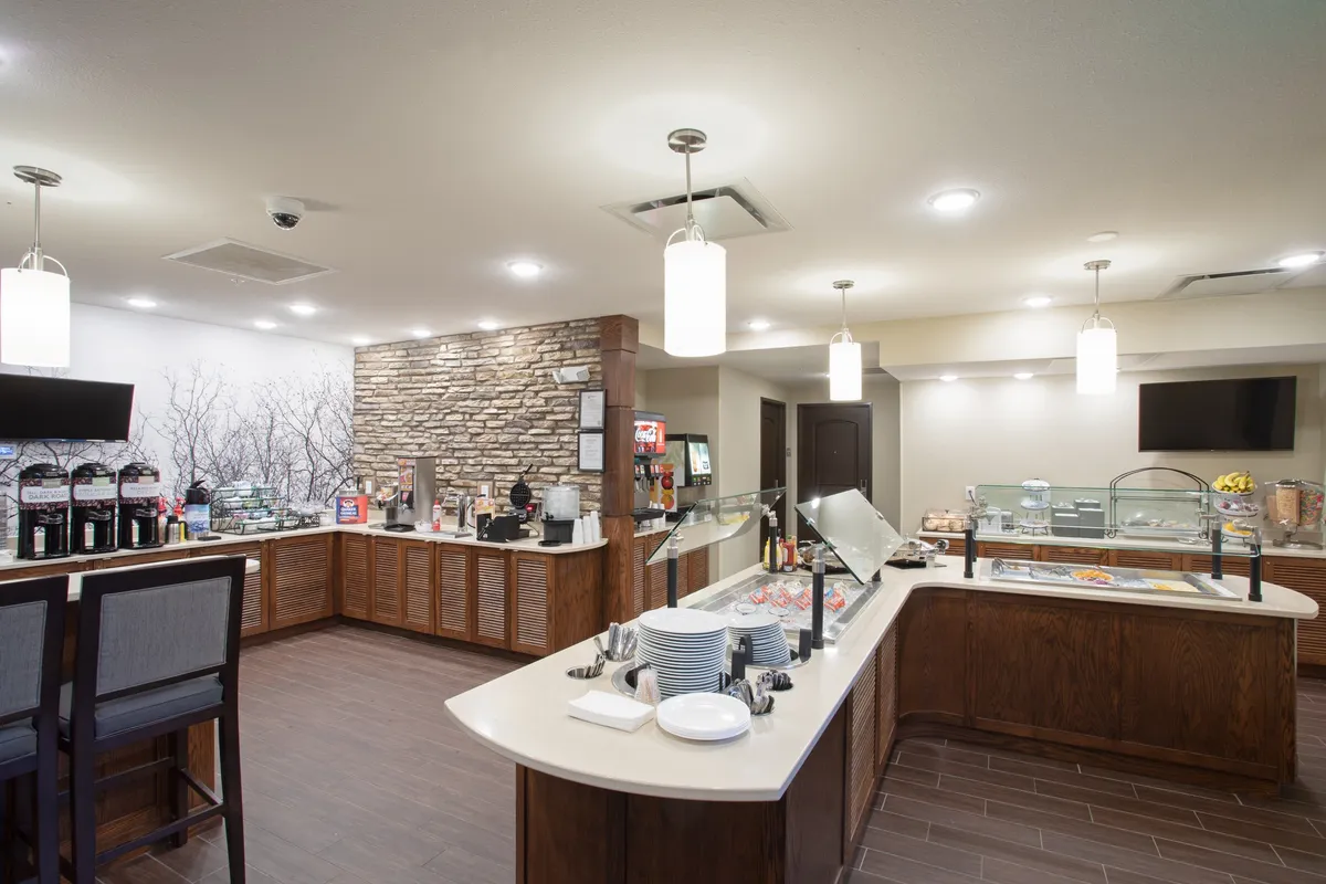 A cozy breakfast buffet station stands against a textured stone feature wall, with a coffee station and a welcoming seating area nearby. The atmosphere is relaxed and inviting, suitable for enjoying a quiet morning or casual conversation.
