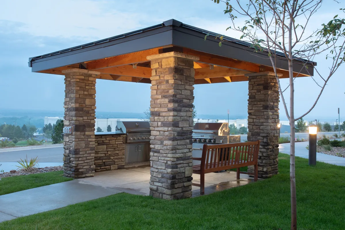 A stone grill area with a wooden bench is nestled within lush greenery, inviting guests to host barbecues or enjoy relaxed social gatherings. The scene emphasizes communal enjoyment in a peaceful, outdoor environment.